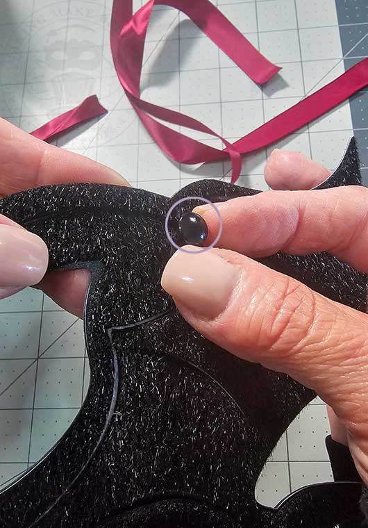 Insert brad fastener through mask layers to secure ribbon tie
